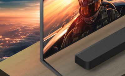 Soundbar diletakkan pada permukaan kayu di bawah TV yang menayangkan pilot yang sedang terbang.