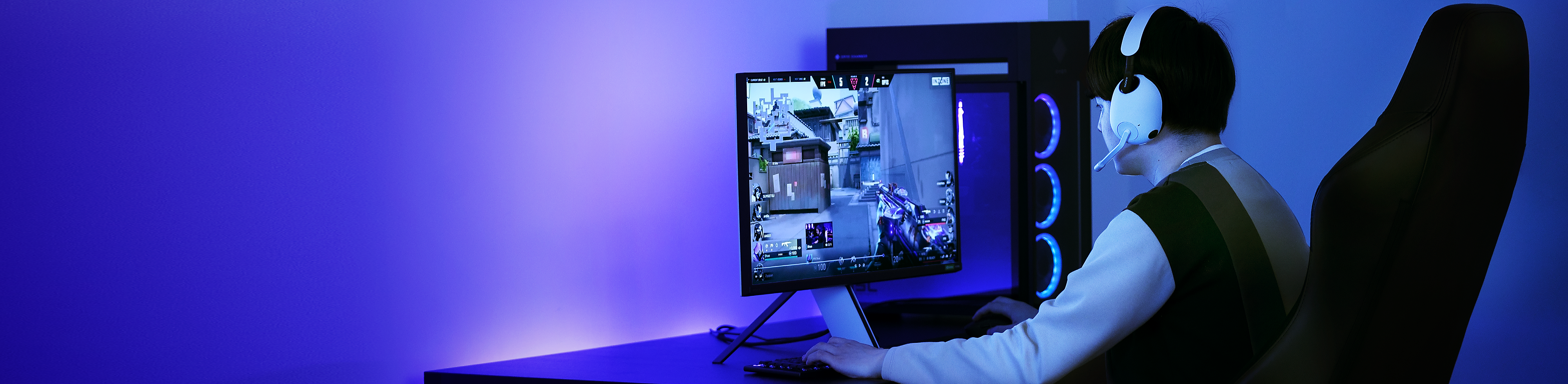 Snímek muže s herní náhlavní soupravou INZONE H9 ve fialově osvětlené místnosti, který na počítači hraje VALORANT