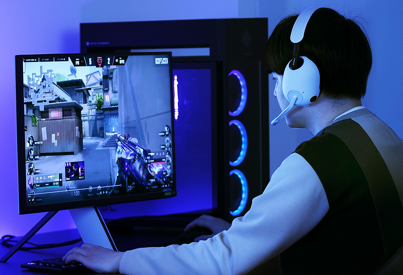 Purpurine šviesa apšviestame kambaryje kompiuteriu VALORANT žaidžiančio ir dėvinčio INZONE H9 žaidimų ausines vyro vaizdas