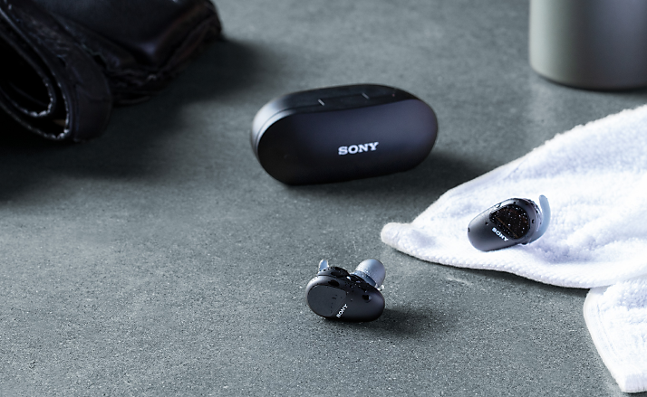 Lifestyle shot of truly wireless sports headphones with a charging case on a dark gray table surface