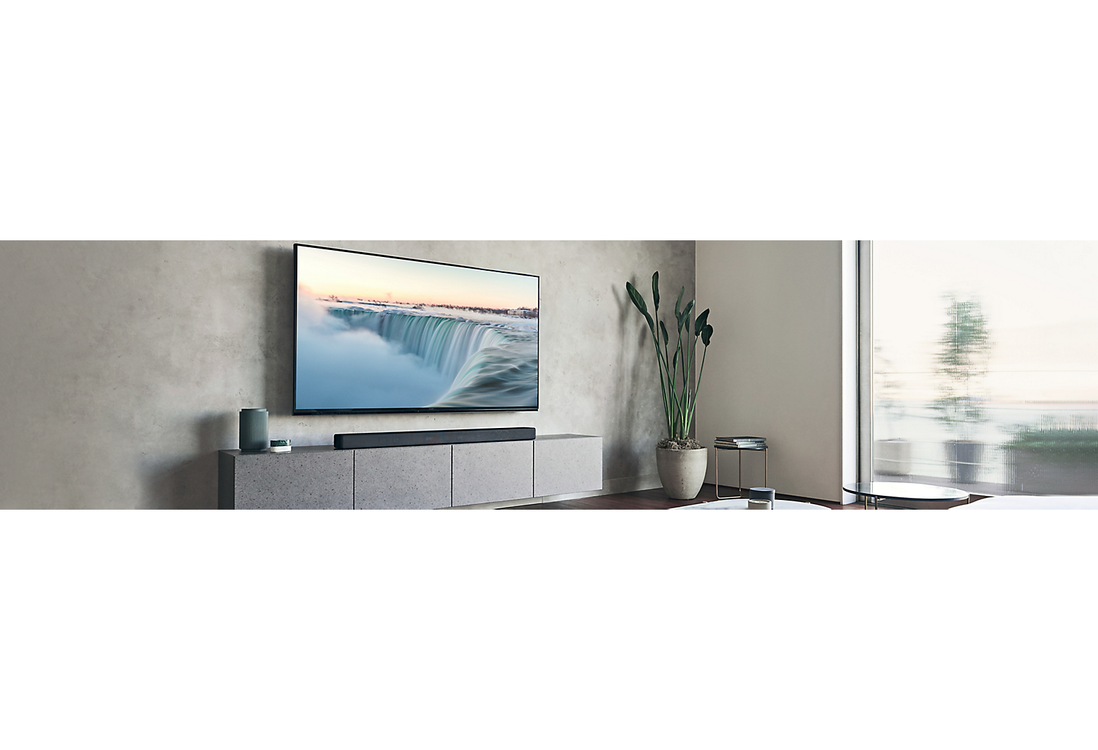 TV montada numa parede cinzenta numa sala de estar em tons cinza com vários artigos de decoração.