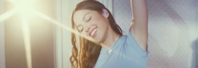 Imagen de Olivia con los auriculares LinkBuds S en violeta puestos en la que levanta un brazo sobre la cabeza con una luz brillante de fondo