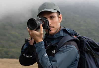 Arka planda bir dağın yer aldığı, fotoğraf makinesi tutan bir adamın durum görüntüsü