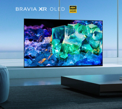 BRAVIA A95K σε πλατφόρμα σε σαλόνι, με τραπέζι και βιβλία στο προσκήνιο και εικόνα με πολύχρωμους μπλε, μοβ και πράσινους κρυστάλλους στην οθόνη