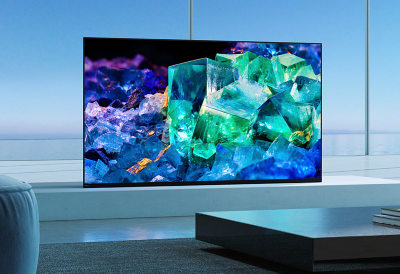 客廳檯上放置著 BRAVIA A95K，前景有桌子與書籍的，螢幕上呈現繽紛的藍色、紫色和綠色玻璃與水晶影像