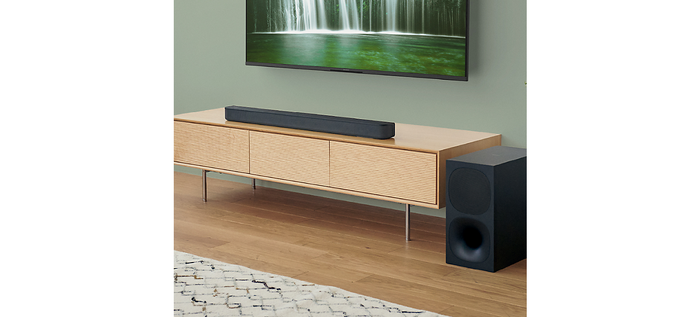 A living room featuring a wall-mounted TV, a soundbar on a cabinet and a wireless subwoofer on the floor
