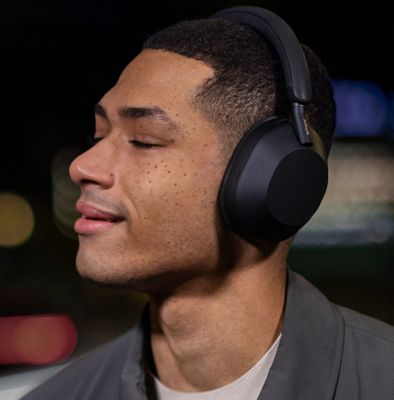 Image of a person listening to a black pair of WH-1000XM5 headphones with their eyes closed and a smile on their face