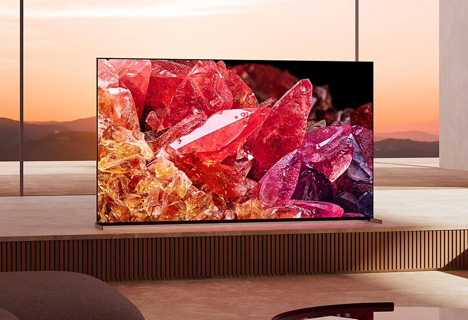 BRAVIA X95K on wooden platform in living room with image of red and orange crystals on screen