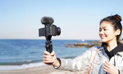 Situational image of a woman taking a selfie with the grip. ECM-G1 is attached on top of the camera.