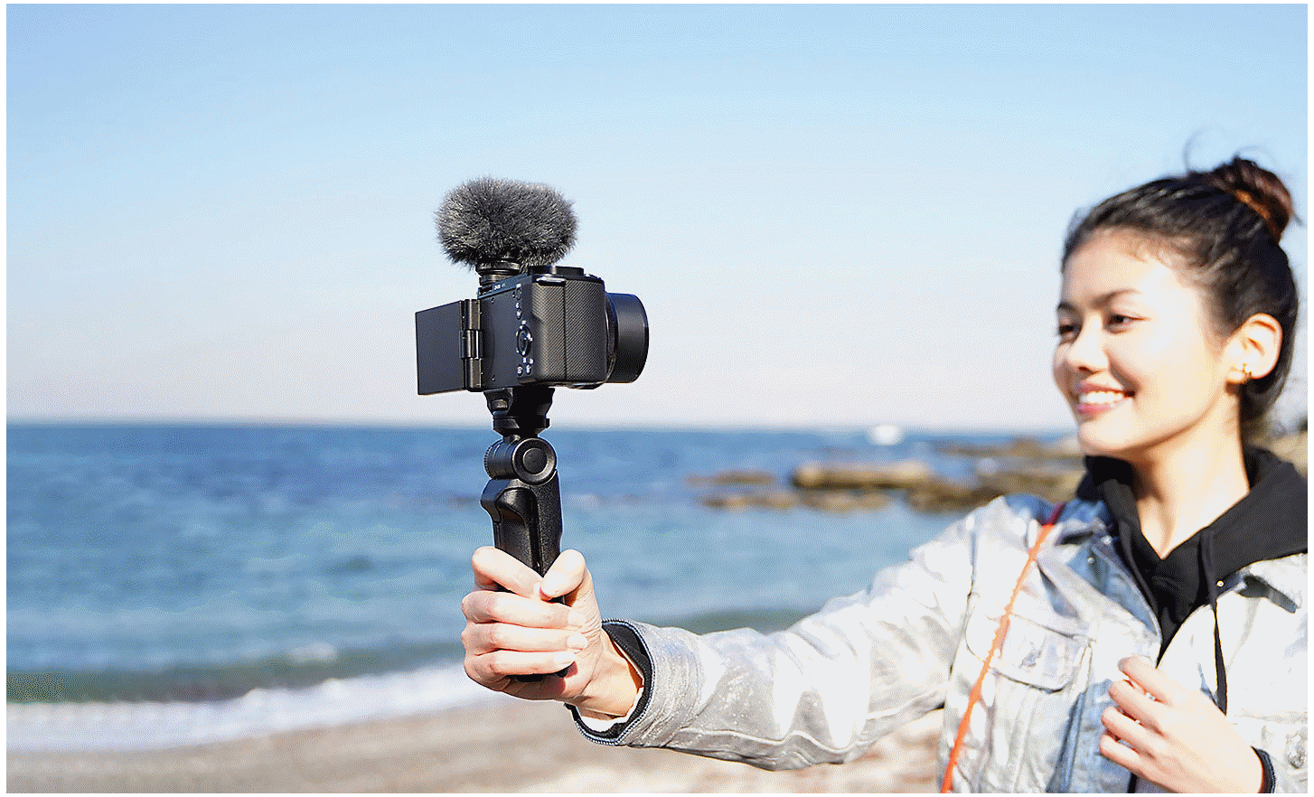 Image situationnelle d'une femme se filmant face caméra avec la poignée. L'ECM-G1 est fixé sur le dessus de l'appareil photo.