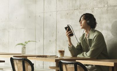 Man wearing headphones using NW‑ZX900 music player seated inside a bright café