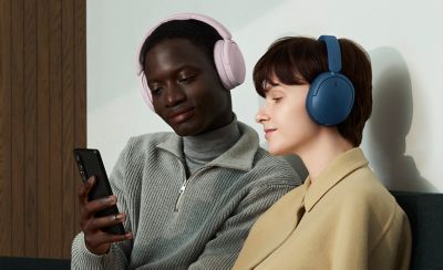 Dos personas en un sofá con unos auriculares WH-CH730N de Sony rosas y azules miran un smartphone