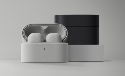  Two sets of wireless earbuds in sleek, textured charging cases. One case is open with white earbuds, and the other is closed and black, on a plain backdrop.