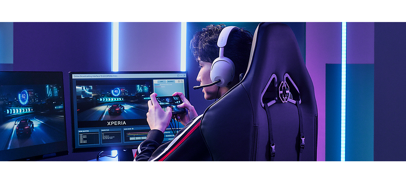 A pro gamer wearing a headset, playing on Xperia 1 IV Gaming Edition connected to two monitors