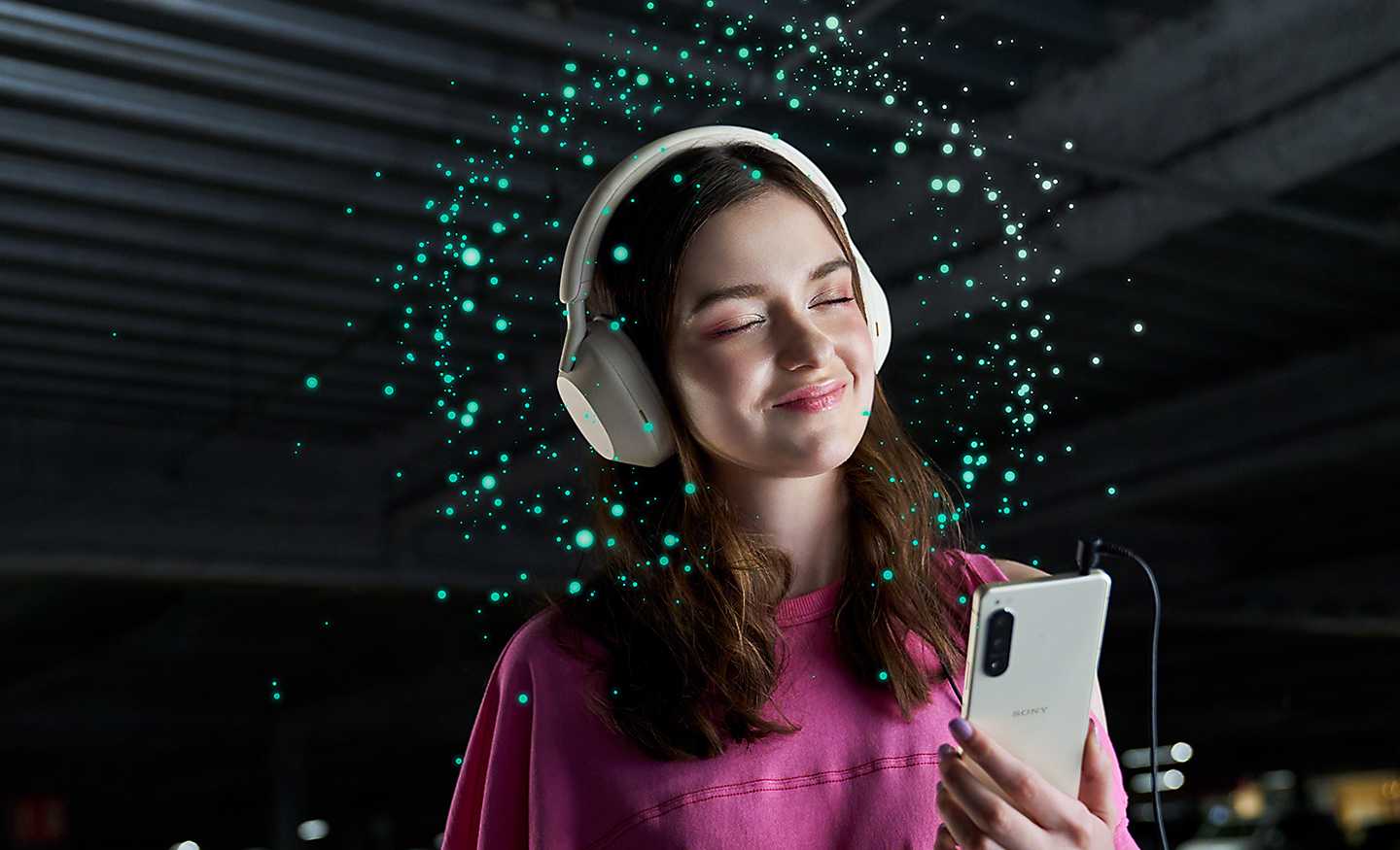 Žena s nasazenými sluchátky poslouchá hudbu na telefonu Xperia 5 IV – kolem hlavy má jiskřivá světla představující technologii 360 Reality Audio