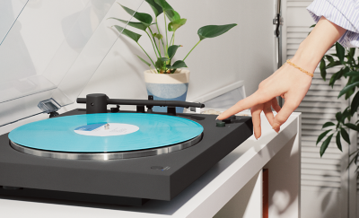 En hand som trycker på en knapp på PS-LX3BT med turkosfärgad skiva