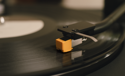 Nahaufnahme des Tonarms und des orangefarbenen Tonabnehmers des Plattenspielers PS-LX5BT, die auf einer sich drehenden schwarzen Schallplatte ruhen.