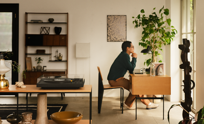 Person, die an einem Schreibtisch im Wohnzimmer sitzt, mit dem Plattenspieler PS-LX5BT im Vordergrund