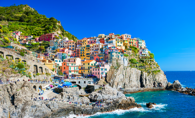 Maisons colorées sur une falaise rocheuse surplombant la mer, avec un ciel bleu clair et des vagues déferlantes en contrebas.