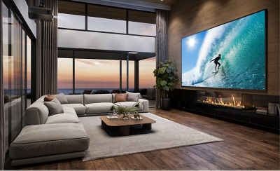 Ceiling-mounted BRAVIA projector showcasing a vibrant surfing scene on a large screen in a luxurious living room, with a modern fireplace and a scenic sunset view.