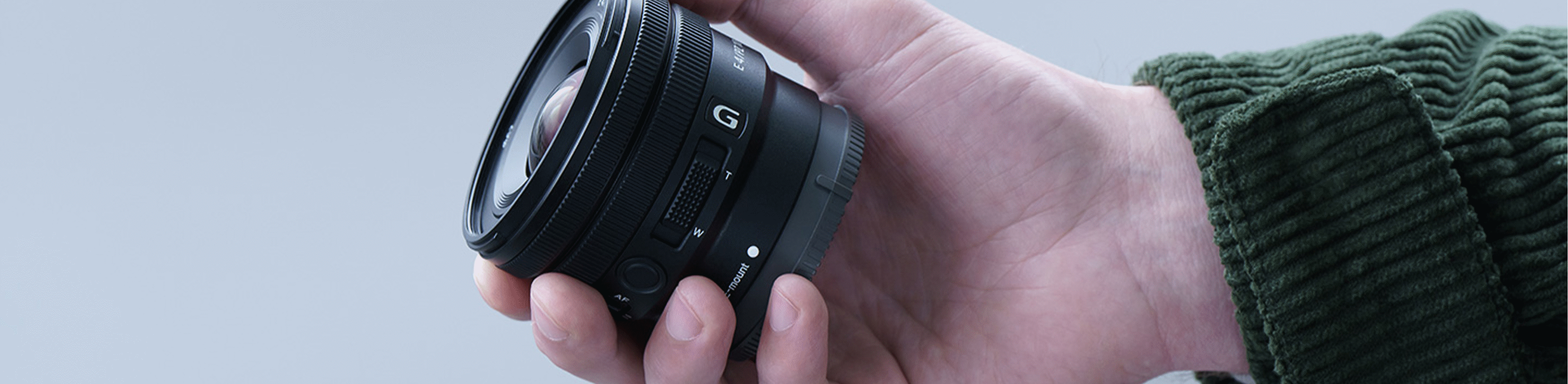 Imagem da mão de uma pessoa a segurar a E PZ 10-20 mm F4 G, mostrando que a lente é suficientemente pequena para caber na mão