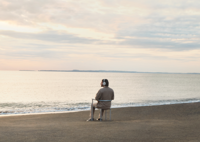 A man in the beach sitting in a chair wearing 1000X THE COLLEXION headphones.