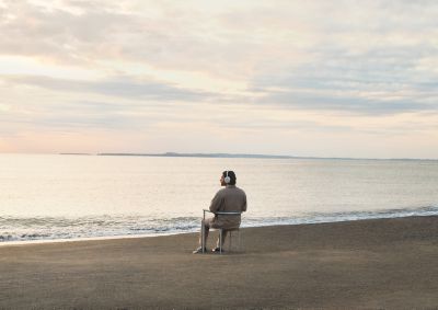 A man in the beach sitting in a chair wearing 1000X THE COLLEXION headphones.