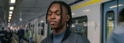 Image of a person with eyes closed, standing on a busy street wearing the WF-1000XM5 headphones