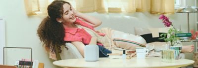 หญิงสาวคนหนึ่งนอนเอนอยู่บนโซฟาโดยมี LinkBuds Speaker อยู่บนโต๊ะกาแฟในฉากหน้า