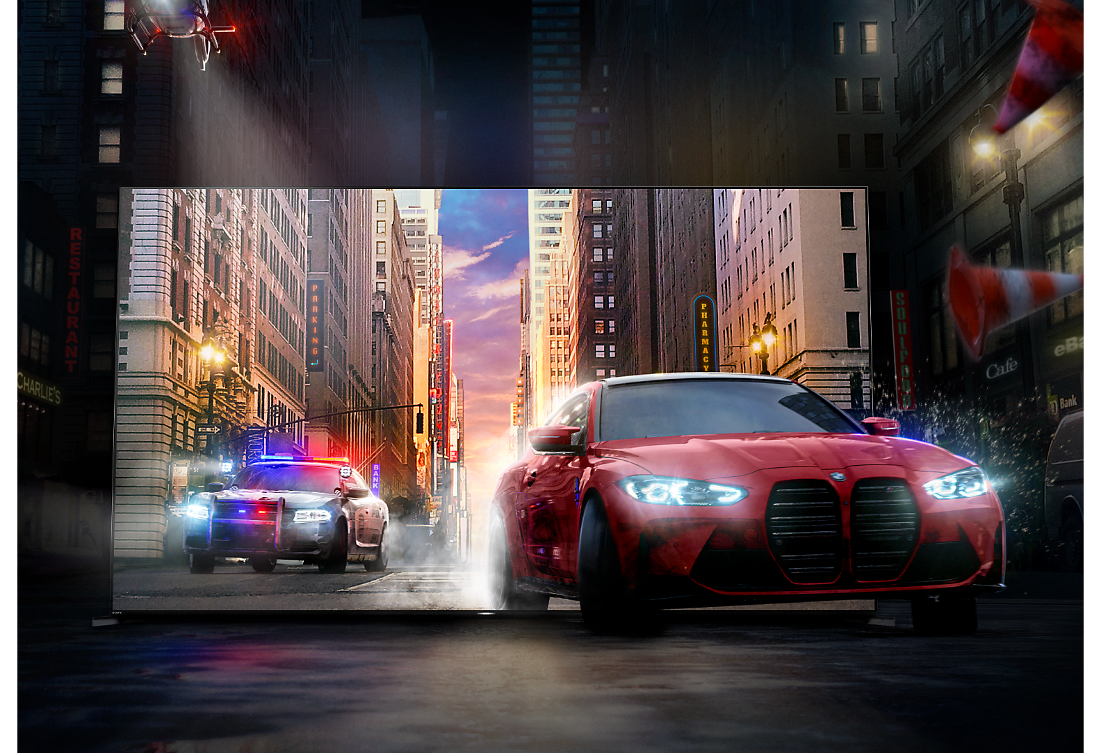 A red car followed by a police car driving out of a BRAVIA TV screen onto a city street