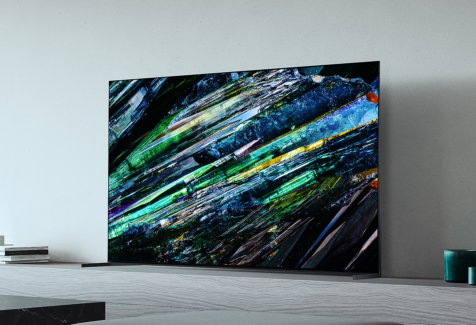 Телевизор BRAVIA A95L с разноцветной иллюстрацией на экране рядом с книгами и растением в гостиной