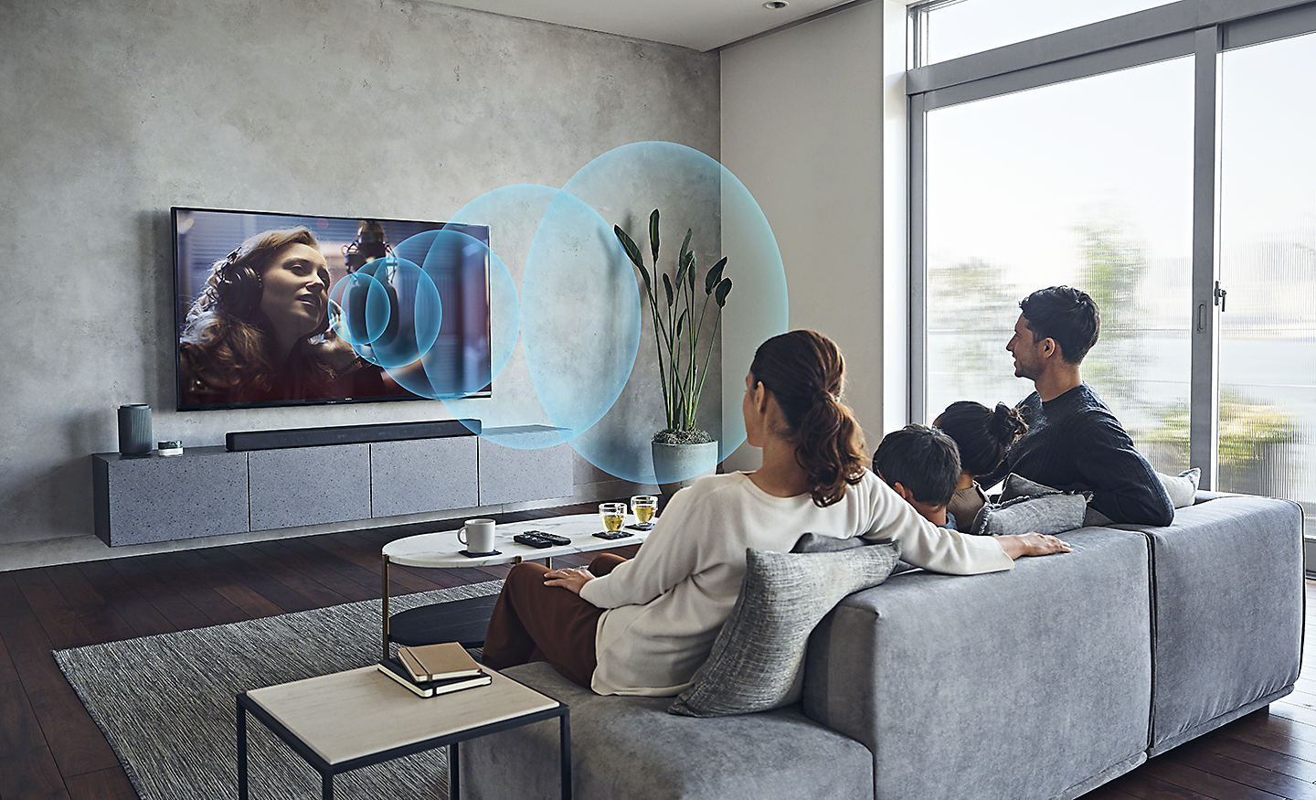 Zdjęcie rodziny przed telewizorem BRAVIA w domowym salonie z ilustrowanymi niebieskimi falami dźwiękowymi symbolizującymi technologię Acoustic Center Sync