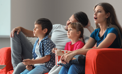 Сім'я з чотирьох людей на дивані, зачарована тим, що дивляться по телевізору