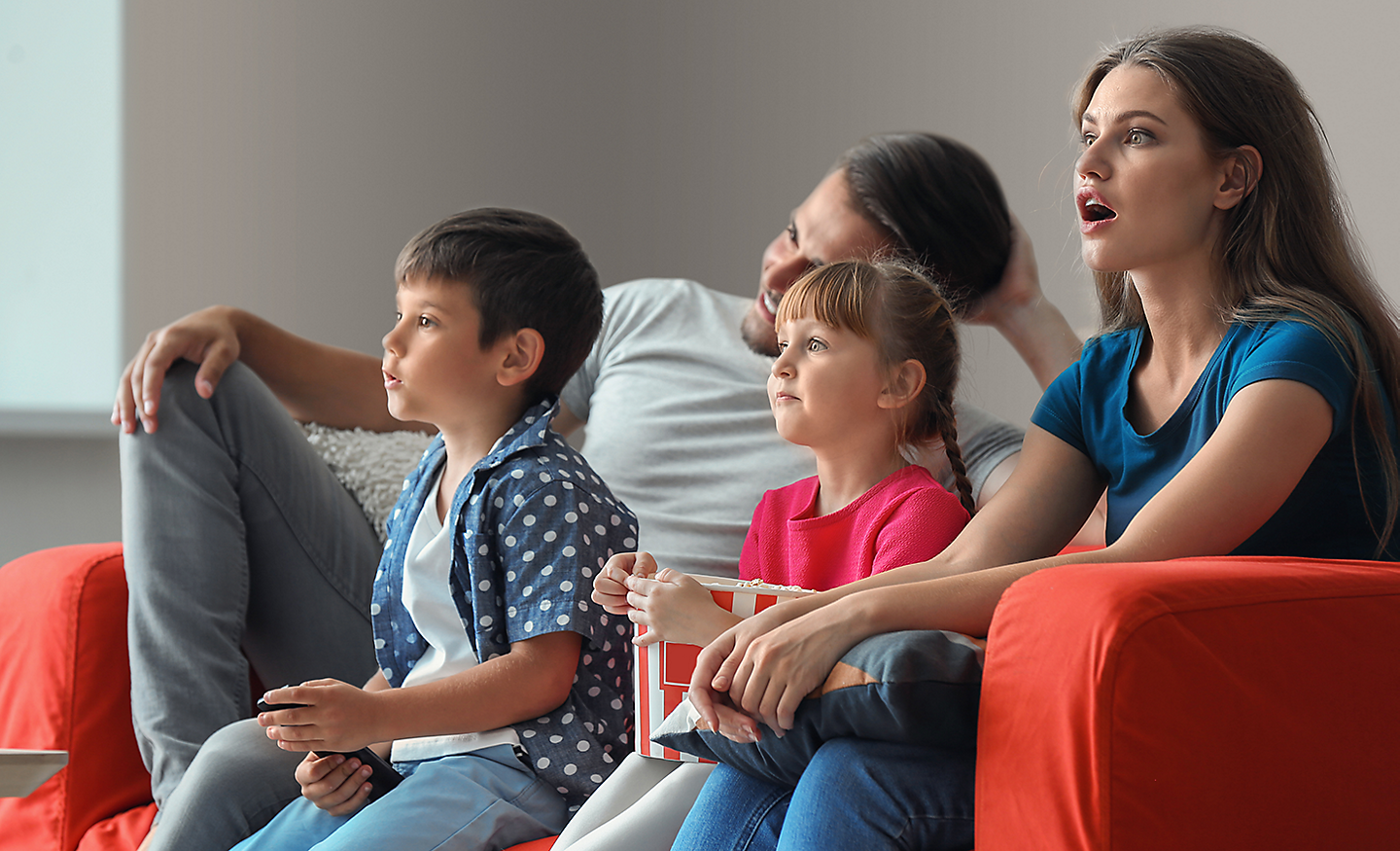 Une famille de quatre personnes sur un canapé, captivées par ce qu'elles regardent sur le téléviseur