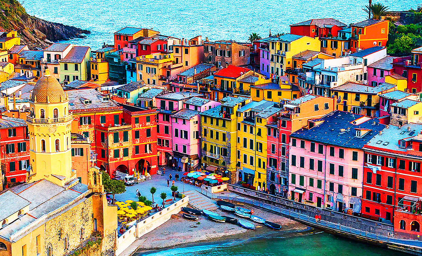 Immagine soleggiata di un piccolo paese di mare con tanti edifici colorati, bar e barche da pesca