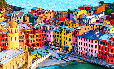 Sunlit image of a small seaside town featuring an array of brightly coloured buildings, cafes and fishing boats