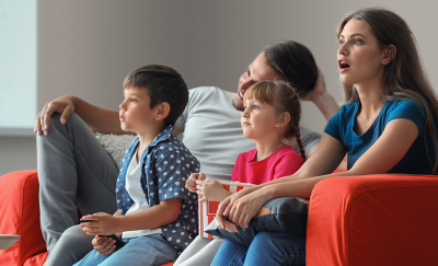 Une famille de quatre personnes sur un canapé, captivées par ce qu'elles regardent sur le téléviseur