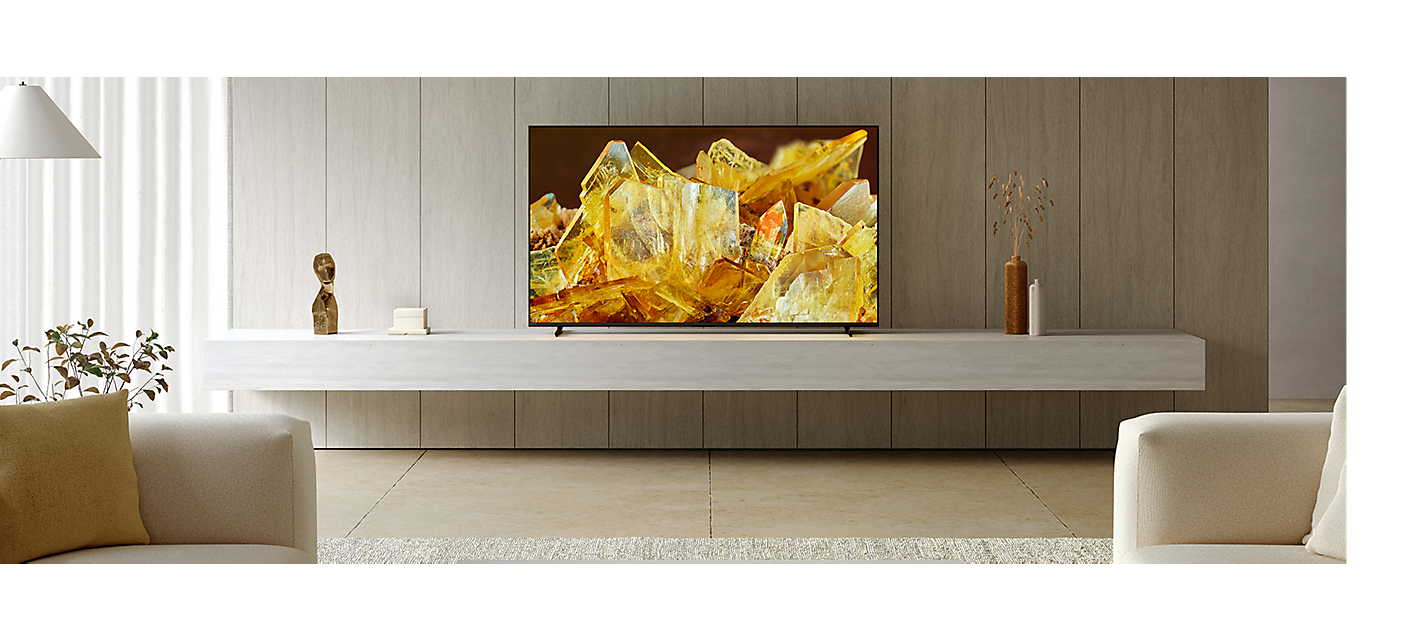 Téléviseur BRAVIA X90L sur un socle avec des cristaux dorés à l’écran, dans un salon