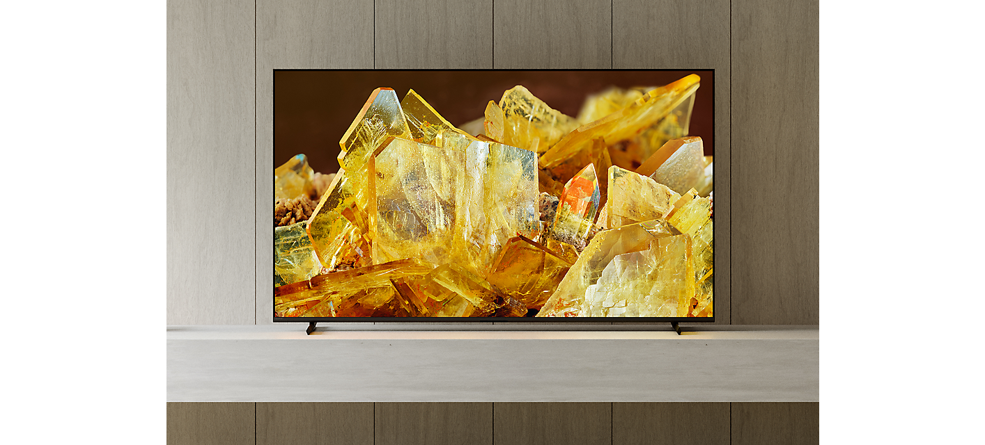 Téléviseur BRAVIA X90L sur un socle avec des cristaux dorés à l’écran, dans un salon