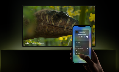 TV treo tường bên trên bệ với ảnh chụp màn hình đầu khủng long và bàn tay cầm điện thoại thông minh ở tiền cảnh, màn hình hiển thị ứng dụng