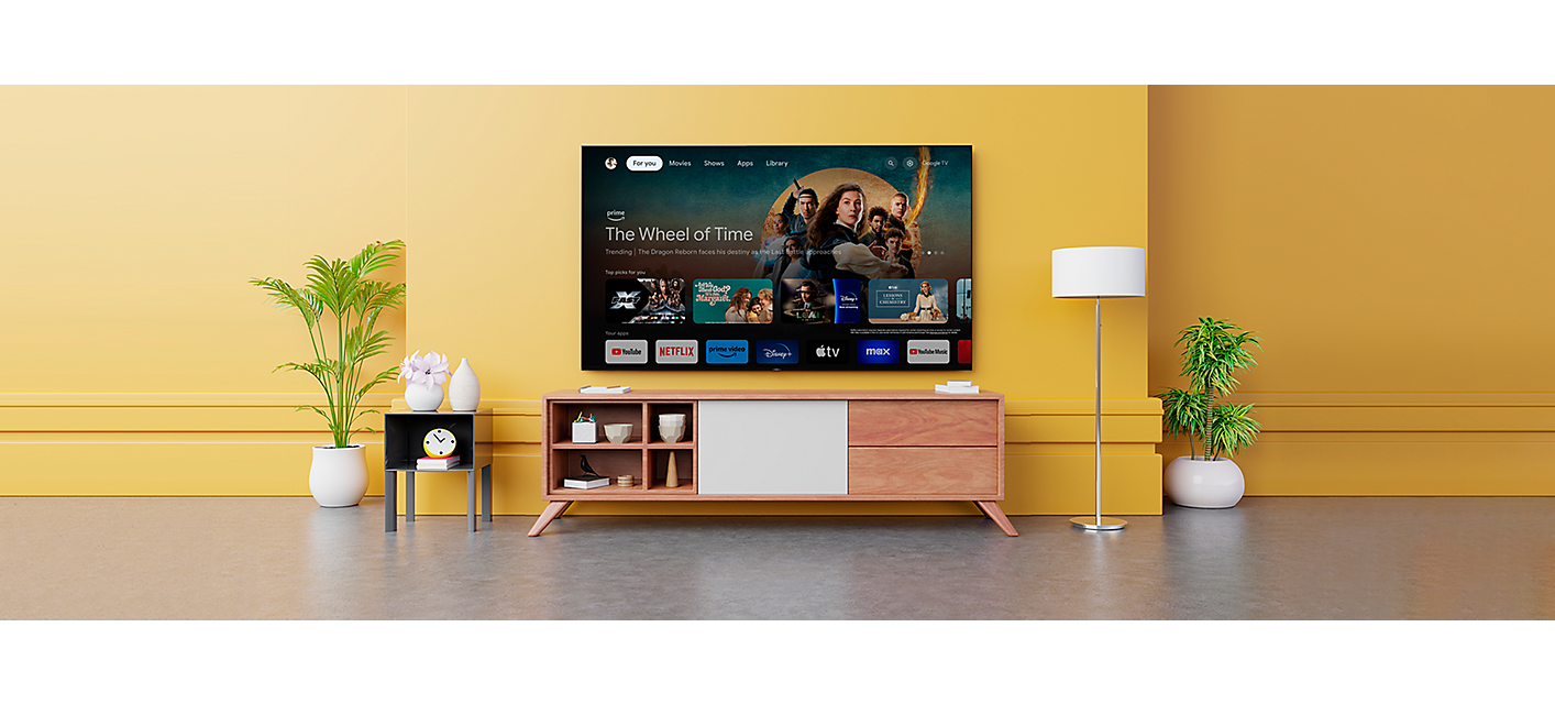 טלוויזיה המותקנת על קיר מעל שידת עץ עם צילום מסך של אפליקציות Google TV