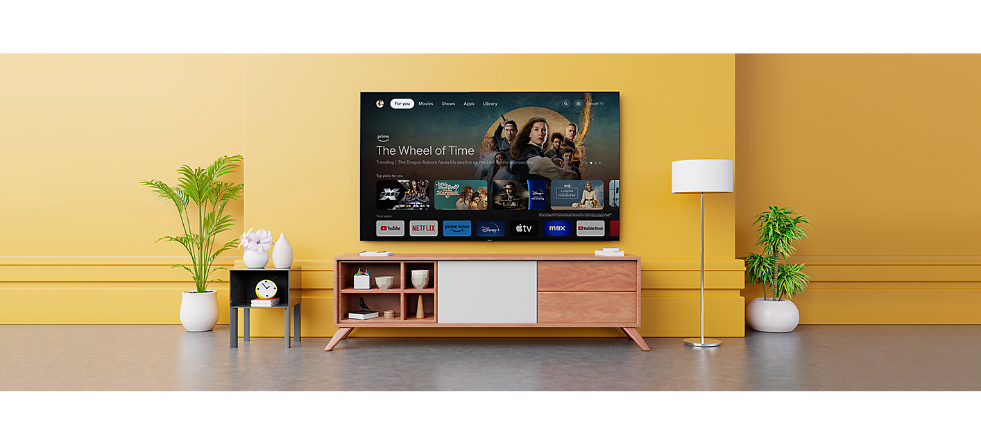 Wall-mounted television above wooden cabinet showing a variety of entertainment apps and selected shows with Google TV logo below left