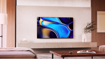 Televizor montat pe perete, deasupra unei polite de marmura, cu o imagine cu picaturi galbene, negre si albastre si o carte pe masa in prim-plan