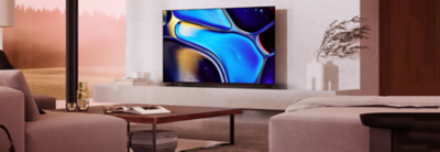 Living room scene with light brown sofa right, coffee table centre with book, and TV on a plinth with ornaments to one side and screenshot of blue water droplets