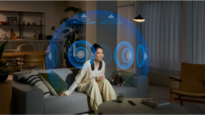 Scena in sufragerie, cu persoana pe canapea, uitandu-se la televizor si purtand BRAVIA Theatre U, cu masuta de cafea in prim-plan si sfera albastra cu difuzoare si efectul de sunet spatial evidentiat