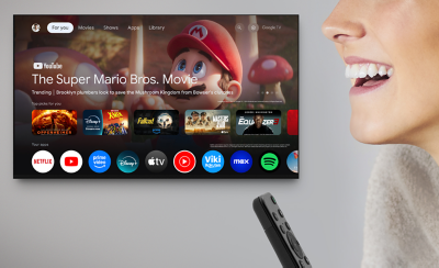 TV treo tường đang hiển thị nhiều ứng dụng giải trí và chương trình tuyển chọn khác nhau, ở bên phải là đầu của một người và điều khiển từ xa.