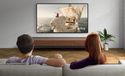 Two people sitting on a sofa watching a wall-mounted TV with screenshot of Lost in Space and Netflix logo bottom right.