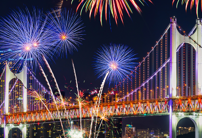 Paisaje urbano en la noche con un puente iluminado y fuegos artificiales.