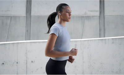 Một người phụ nữ áo trắng đang chạy bộ ngoài trời với tai nghe màu trắng trên tai.