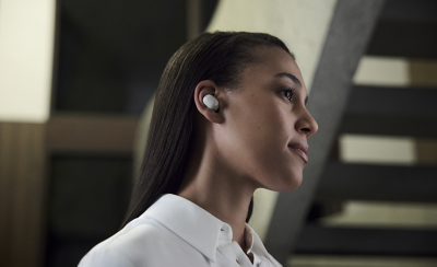 Ảnh chụp góc nghiêng một người phụ nữ đeo tai nghe màu trắng, mặc áo sơ mi trắng trong một tòa nhà hiện đại.